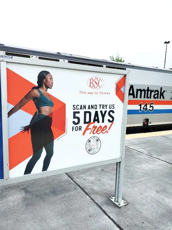 BSC platform ad beside an Amtrak train: scan and try us 5 days for free