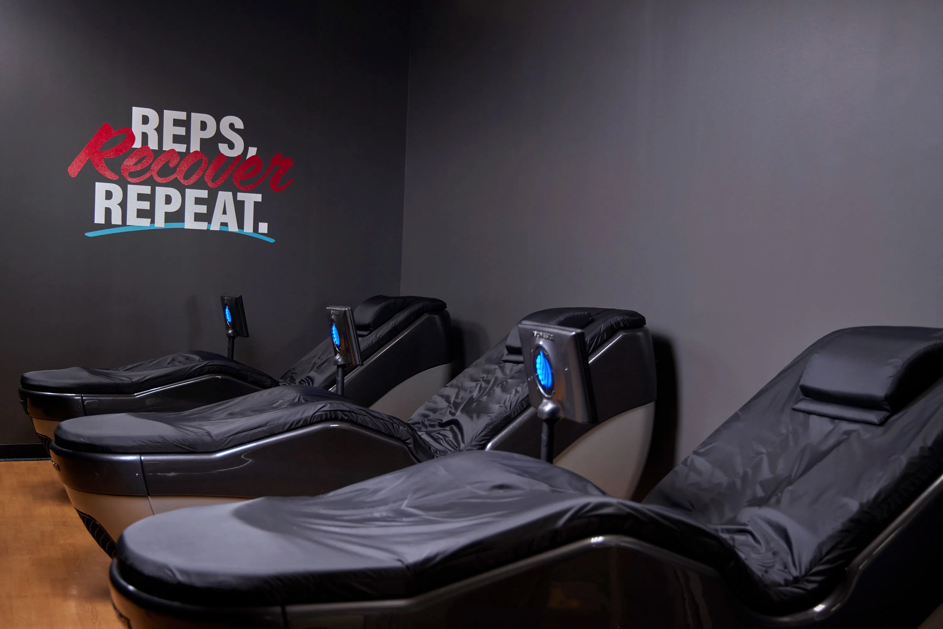 Recovery room with massage chairs under a Reps, Recover, Repeat wall graphic