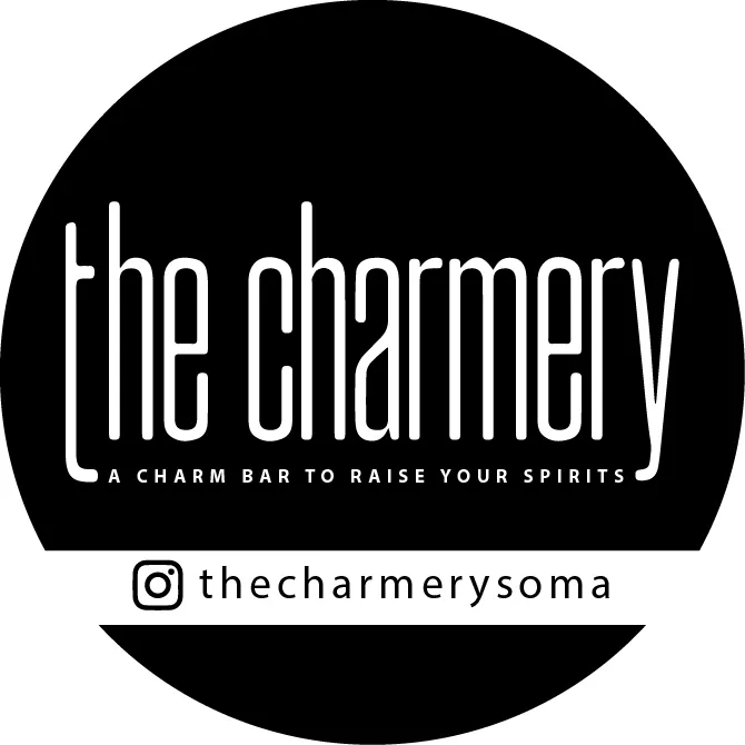 The Charmery logo in a black circle with the tagline A charm bar to raise your spirits and the thecharmerysoma Instagram handle